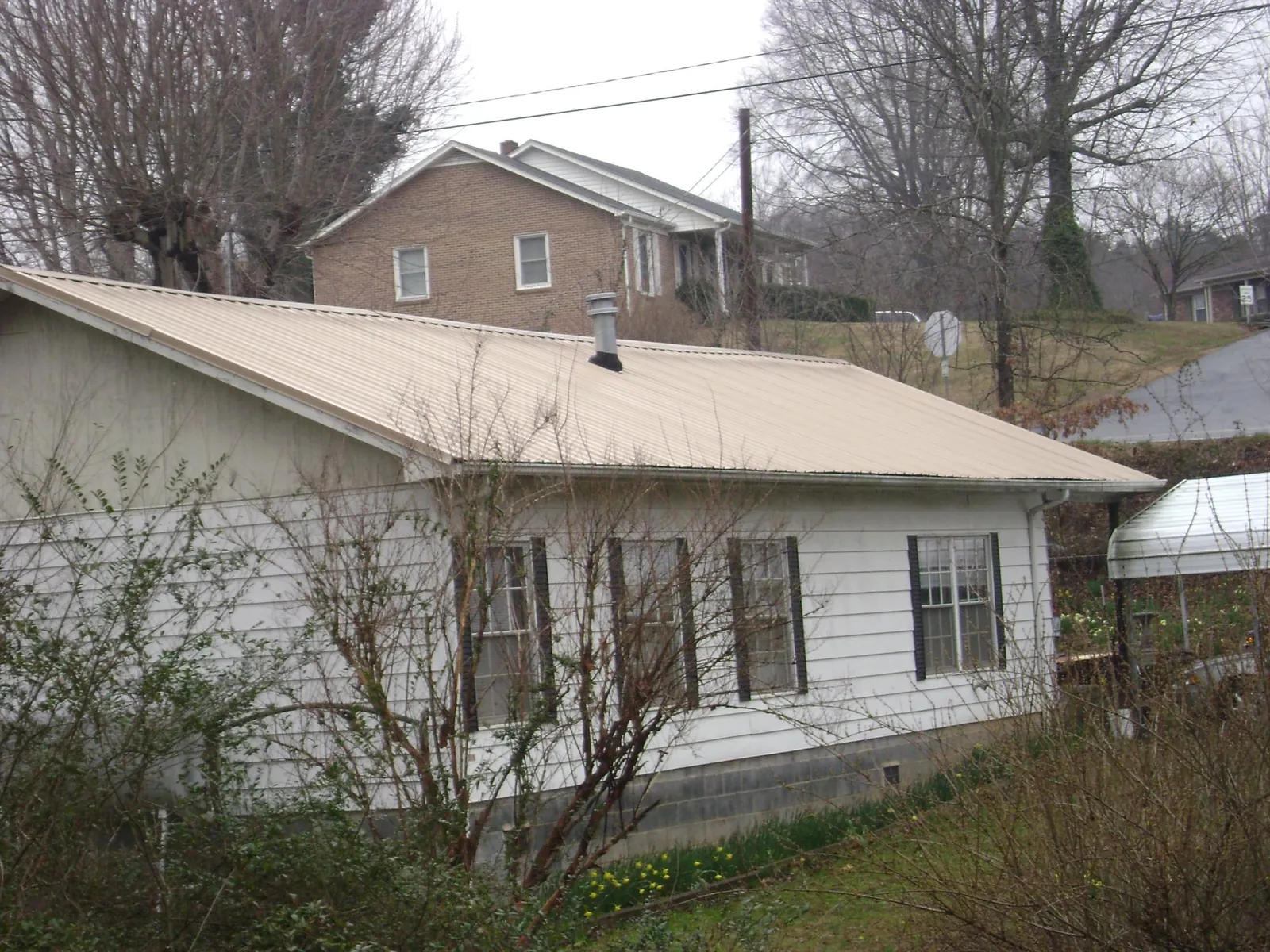 Tan metal roof on a white sided house set into a hillside — Commercial Roofing by Roofing Brothers in Woodstock